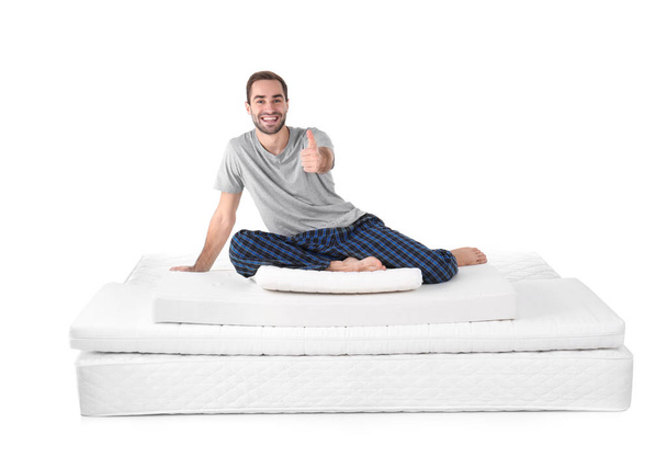 Young man sitting on mattress pile against white background - Fotó, kép