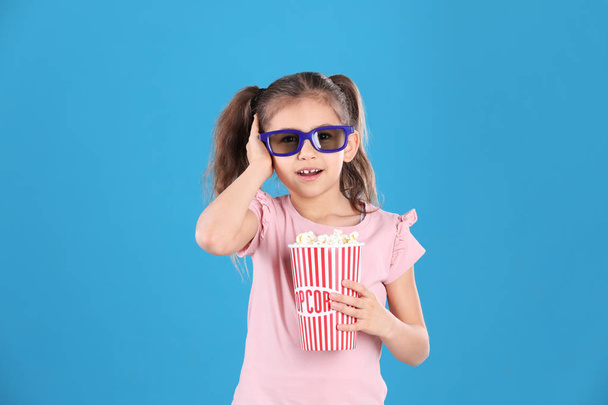 Cute little girl with popcorn and glasses on color background - 写真・画像