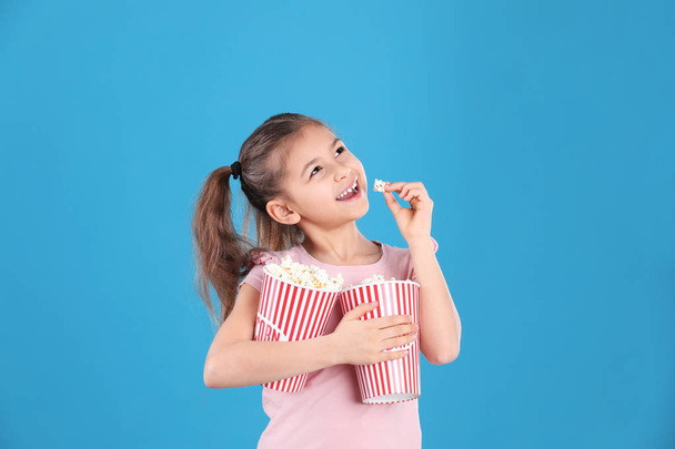 Cute little girl with popcorn on color background - Photo, image