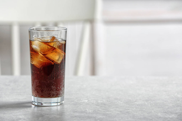 Glass of cold cola on table against blurred background. Space for text - Foto, afbeelding