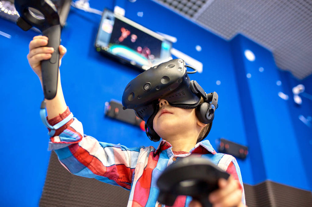 modern technology, gaming and people concept - boy in virtual reality headset or 3d glasses playing videogame at game centre - Foto, imagen
