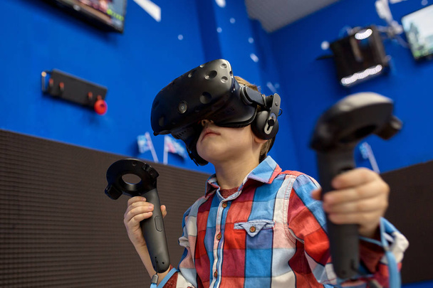 modern technology, gaming and people concept - boy in virtual reality headset or 3d glasses playing videogame at game centre - Foto, Imagen