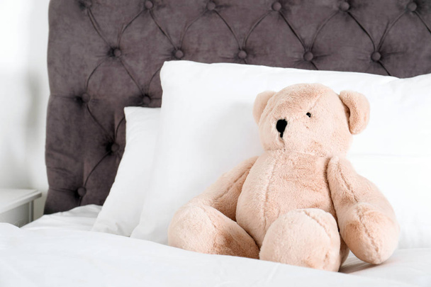 Cute teddy bear sitting on bed indoors. Space for text - 写真・画像