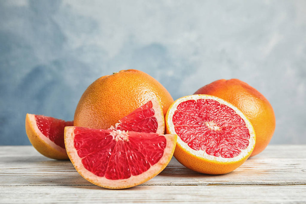 Composition with yummy grapefruits on wooden table against color background - Фото, зображення