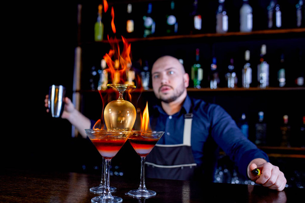 Vurige Toon aan de bar. De barman maakt hete alcoholische cocktail en ontbrandt bar. Bartender bereidt een vurige cocktail. Brand op balk. - Foto, afbeelding