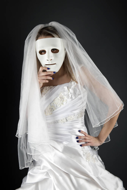 Gyönyörű szőke menyasszony fehér ruhában, fehér maszk mögé bújva. - Fotó, kép