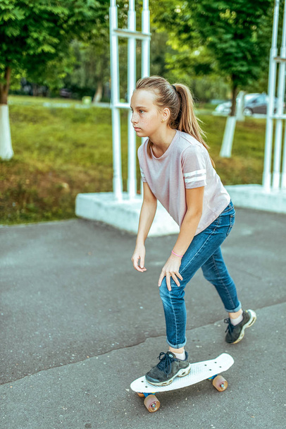 Girl teenager 10-15 years old, riding a skateboard. In the summer in the city in casual jeans and sneakers. Walk in the summer park, after school lessons, rest in the city. - 写真・画像