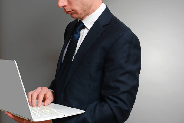 Mies puvussa kirjoittamassa pitäen kannettavaa tietokonetta
 - Valokuva, kuva