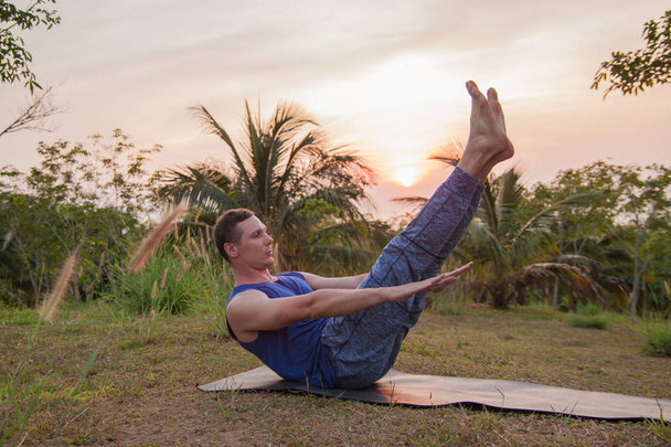  gün batımında Yoga palmiye ağacı yakınındaki yapan genç erkek. - Fotoğraf, Görsel