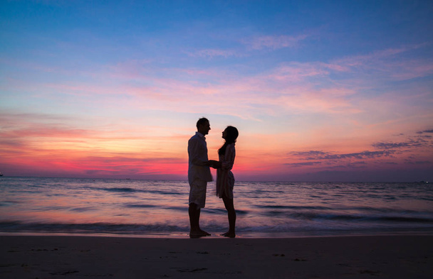 Silhouette eines verliebten Paares, das sich bei Sonnenuntergang am Meer an den Händen hält. - Foto, Bild