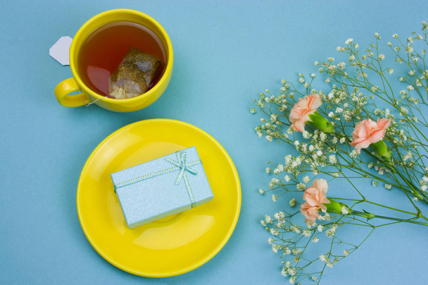 top view tea cup with tea bag,gift box on a plate and bouquet of flowers on a pastel blue background - Foto, Bild