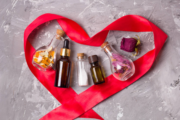Spa concept of love for your body: heart shaped red satin ribbon aroma oils bottles,sea solt, dry rose petals and orange peel for scrub - Foto, Imagem
