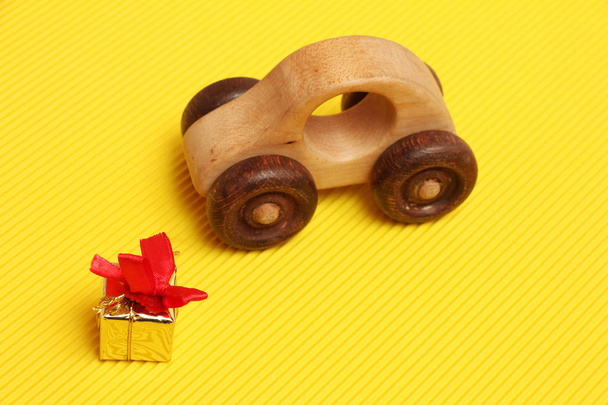 wooden car toy and golden gift box with red ribbon on corrugated yellow background, present for fathers day or birthday  - Photo, Image