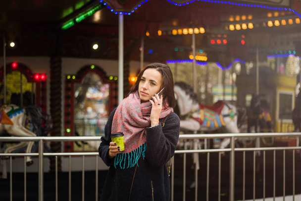 sad young woman talking on the phone on a blurred carusel background. - Foto, afbeelding