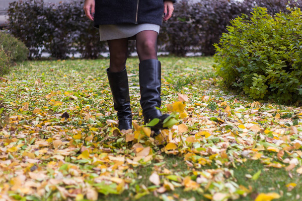 woman in leather boots walking in the park and kicking autumn leaves - Foto, afbeelding