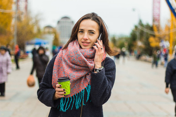 young beautiful brunette girl with  coffee to go  and smartphone on the background of blurred city  street - Фото, зображення
