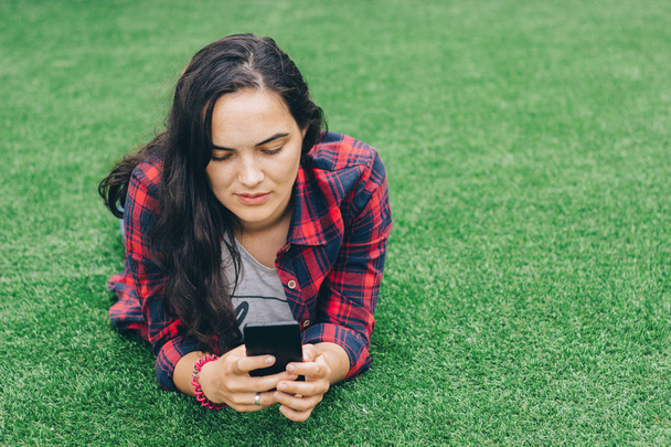 молода дівчина студент лежить на траві з телефоном в руці
. - Фото, зображення