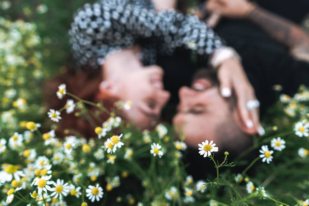 Молодая пара лежит на поле с маргаритками
. - Фото, изображение