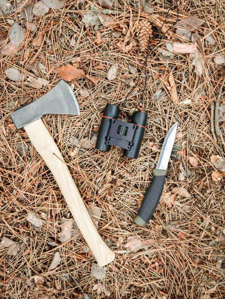 hacha, prismáticos y cuchillo turístico en el suelo cubierto de agujas de pino
 - Foto, imagen