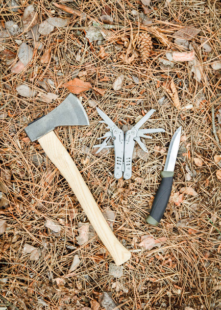 sekera a turistické nože jako multitool na zemi pokryté borovým jehličím - Fotografie, Obrázek