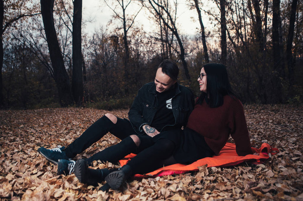 young man and young woman are sitting on a plaid in an autumn fo - Фото, зображення