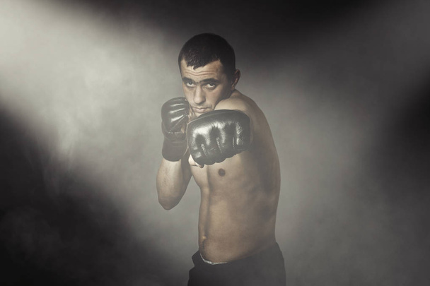 Un homme en gants pour se battre sans règles MMA sur fond noir. Concept d'entraînement, entraînement au combat, coup de pied pratique
 - Photo, image