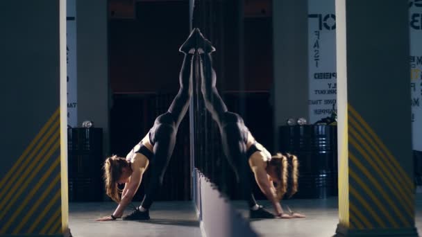 Stretching gymnast blonde pretty woman with attractive body, in leggings, black top and sneakers , doing vertical split, twine, with one foot on wall and other on the floor. she moves very excitingly - Кадры, видео