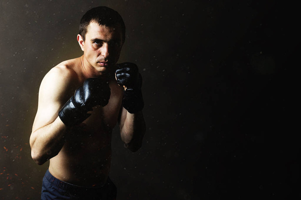Een man in handschoenen voor vechten zonder regels Mma op een zwarte achtergrond. Training concept, combat training - Foto, afbeelding