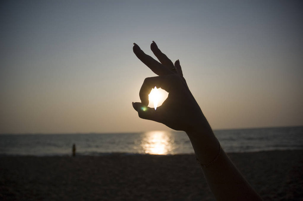sun in a woman's hand as an OK sign overlooking the ocean - Photo, Image
