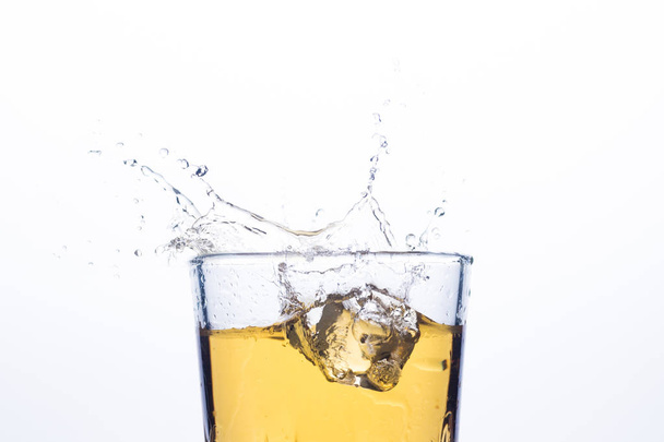 Splash of whiskey from ice cubes on a white background. Concept of alcoholic drinks with ice, whiskey or brandy, apple juice and cooling drinks - Foto, Imagem