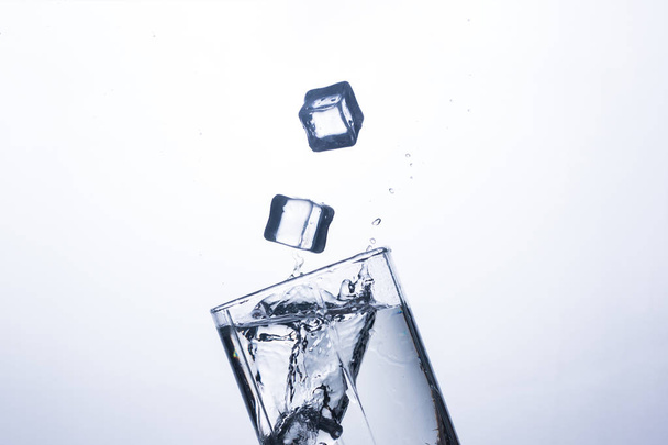 Um respingo de água em um copo de um cubo de gelo em um fundo branco. O conceito de saciar a sede e refrigerar bebidas em tempo quente. Balanço hídrico e consumo diário de água
 - Foto, Imagem
