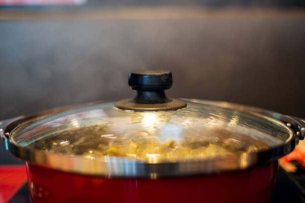 Sopa fervente em panela vermelha com fumaça na mesa
 - Foto, Imagem