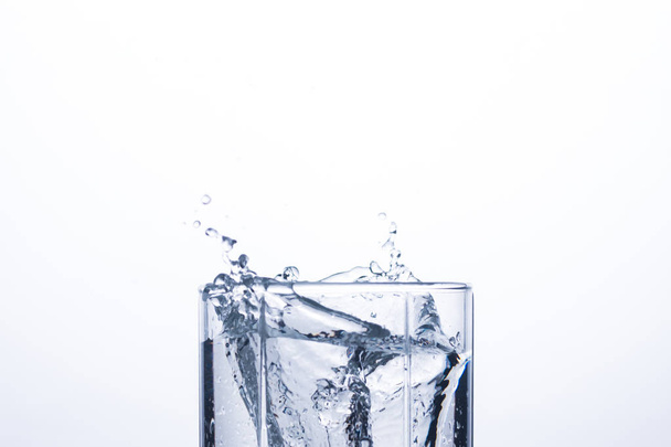 Šplouchání vody ve sklenici z kostku ledu na bílém pozadí. Pojem uhasit žízeň a chlazení nápojů v horkém počasí. Vodní bilance a denní spotřeba vody - Fotografie, Obrázek