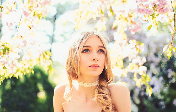 Girl on dreamy face, tender blonde looks at camera, nature background, defocused. Tenderness concept. Young woman enjoy nature in garden. Lady walks in park on sunny spring day. - Foto, afbeelding