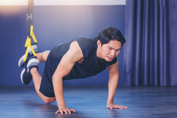Hombre en forma haciendo ejercicio de tablón para la columna vertebral posterior mediante flexiones con correas de fitness de cuerda en el gimnasio
 - Foto, Imagen