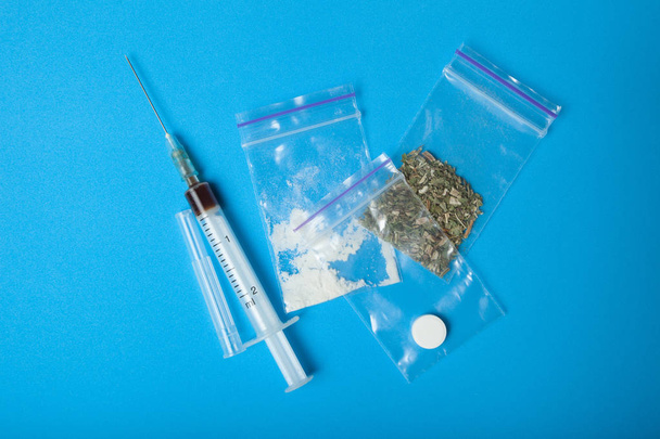 A syringe and a set of illegal drugs in doses on a blue backgrou - Foto, immagini
