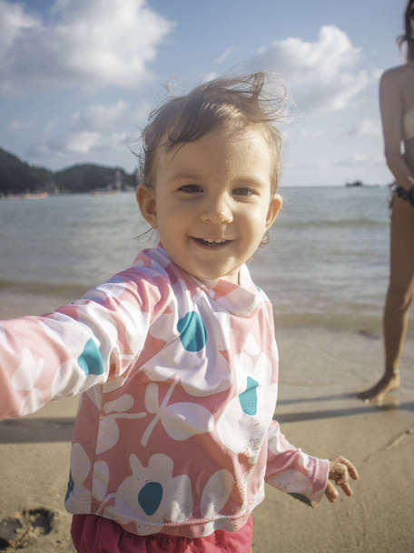 Kızı bir paketle ayakta sahilde veren anne zevk A yaz gün On The Beach ve yüzme poolmother. - Fotoğraf, Görsel