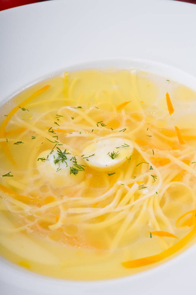 Zuppa di spaghetti gialli servita con uovo di quaglia in piatto bianco
 - Foto, immagini
