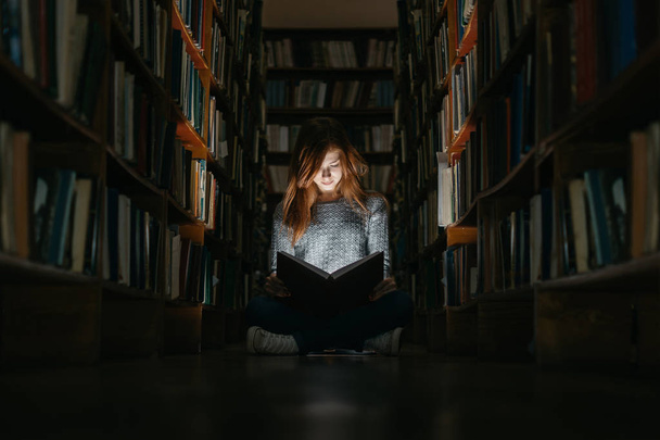 Mädchen liest ein Büchlein in der öffentlichen Bibliothek auf dem Fußboden sitzend. das Mädchen in der öffentlichen Bibliothek - Foto, Bild