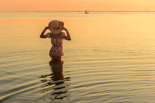 beautiful woman in broad-brim posing in the ocean at amazing sun - Фото, изображение