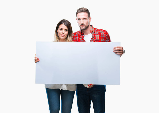 Young couple together holding blank banner over isolated background with a confident expression on smart face thinking serious - Фото, изображение