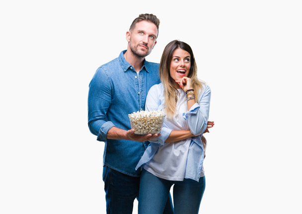 Young couple in love eating popcorn over isolated background serious face thinking about question, very confused idea - Photo, image