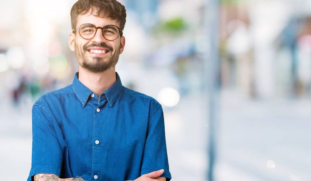Young handsome man wearing glasses over isolated background happy face smiling with crossed arms looking at the camera. Positive person. - Valokuva, kuva