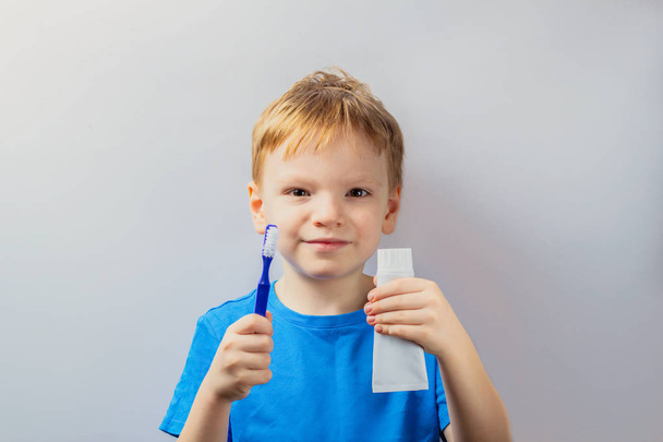 Il bambino tiene in mano uno spazzolino, un dentifricio e sorride felicemente.
. - Foto, immagini