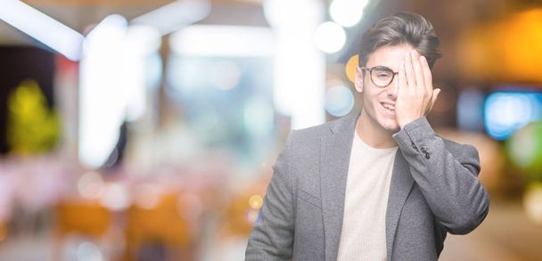 Mladí obchodní muž nosí brýle izolované pozadí zahrnující jedno oko rukou s sebejistý úsměv na tvář a překvapení emoce. - Fotografie, Obrázek