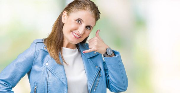 Красивая зрелая женщина средних лет в модной кожаной куртке на изолированном фоне улыбается, делая телефонный жест с рукой и пальцами, как говорить по телефону. Коммуникационные концепции
. - Фото, изображение