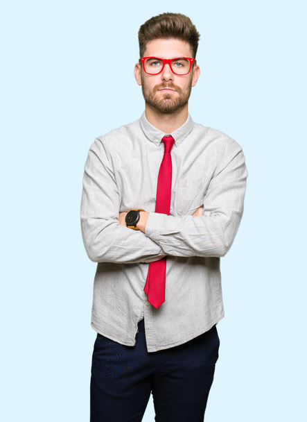 Young handsome business man wearing glasses skeptic and nervous, disapproving expression on face with crossed arms. Negative person. - 写真・画像