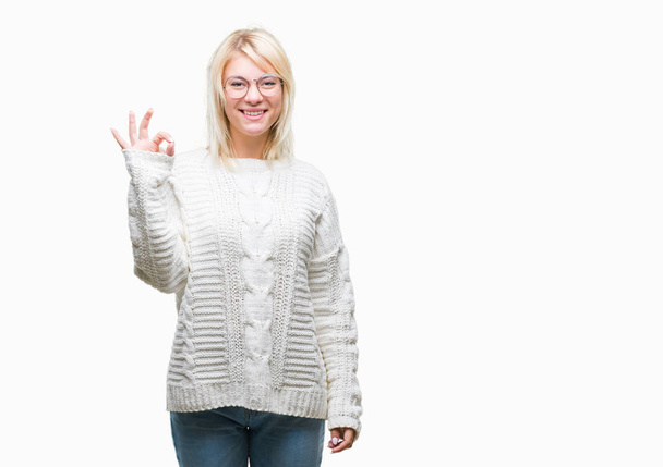 Молода красива блондинка в зимовому светрі і окулярах над ізольованим тлом посміхається позитивно, роблячи знак ок з рукою і пальцями. Успішний вираз
. - Фото, зображення