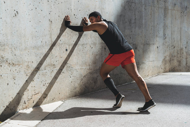 Мужчина бегун делает упражнения на растяжку, готовится к утренней тренировке на открытом воздухе
. - Фото, изображение