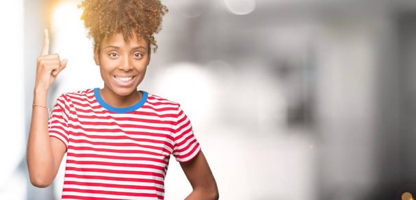 Mooie jonge Afro-Amerikaanse vrouw op geïsoleerde achtergrond vinger omhoog met succesvolle idee. Verlaten en gelukkig. Nummer één. - Foto, afbeelding